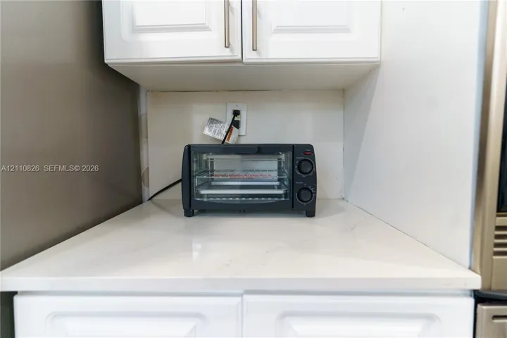 White shaker-style cabinetry with metallic pulls, stone-surface countertop, and smooth-finish backsplash
