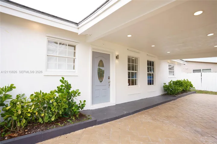 Exterior entry featuring a covered carport with recessed lighting, a paver driveway, an oval-inset front door, and manicured landscaping