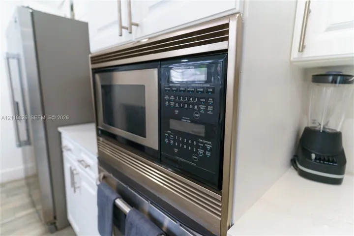 Built-in stainless steel microwave oven, white cabinetry featuring brushed metal hardware, and solid-surface countertops