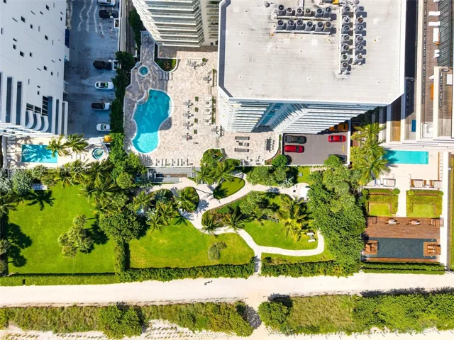 Aerial perspective featuring a swimming pool, integrated spa, expansive landscaped green space with manicured lawn, stone-paved patio, and established palm trees