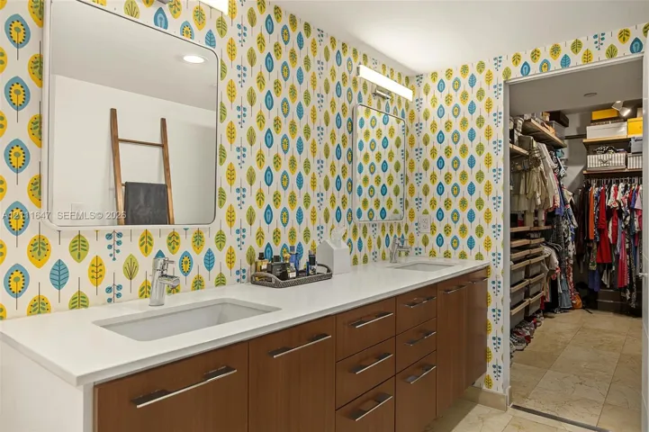 Dual-vanity cabinetry with wood-finish drawer fronts, rectangular undermount sinks, stone countertops, and wall-mounted light fixtures