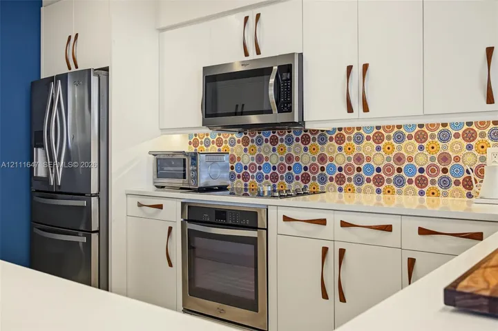 Kitchen featuring white cabinetry with wood-finish hardware, patterned tile backsplash, quartz countertops, and stainless steel appliances