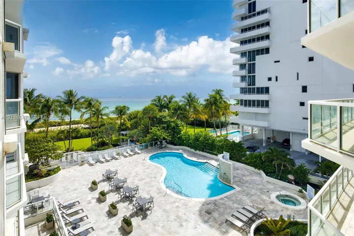 Outdoor swimming pool and spa surrounded by a stone-paved deck, landscaped grounds, and ocean scenery