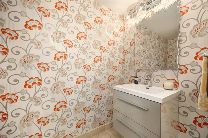 Wall-mounted vanity with a rectangular sink, patterned wallpaper, and a decorative-edge mirror with integrated three-bulb light fixture