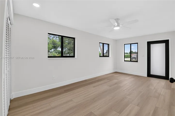 Light-filled room featuring wood-finish flooring, recessed lighting, a modern ceiling fan, multiple windows with black framing, and a frosted glass exterior door
