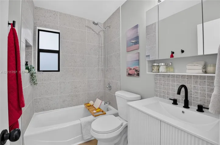 Bathroom featuring a white vanity with a rectangular sink, matte black fixtures, full-width mirrored medicine cabinet, a tiled shower surround with a built-in recessed niche, and a neutral-toned tile backsplash