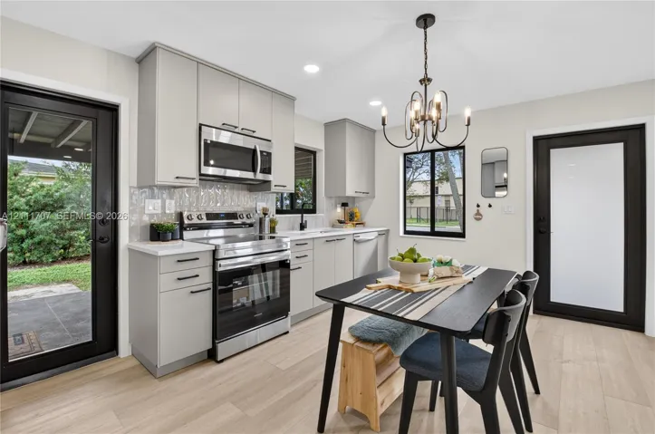 Kitchen featuring beige flat-panel cabinetry, stainless steel appliances, a textured tile backsplash, wood-finish flooring, and a multi-light chandelier