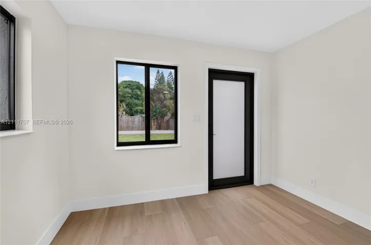 Interior space featuring neutral-toned walls, wood-finish flooring, black-framed windows, and a black-framed door with a frosted glass panel
