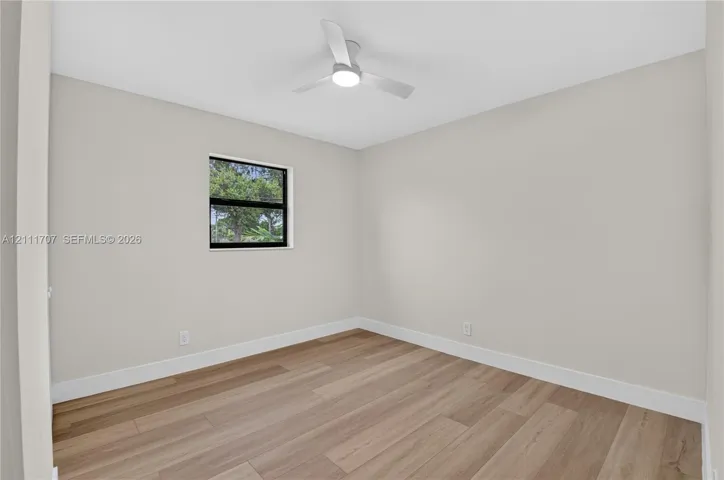Neutral-toned walls, wood-finish flooring, and a modern ceiling fan with integrated lighting, featuring a single window with black framing