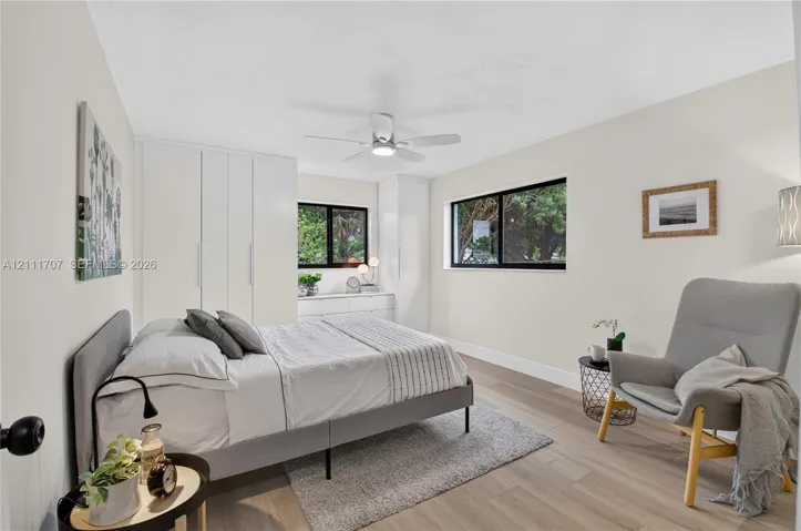 Bedroom featuring wood-finish flooring, floor-to-ceiling built-in closet cabinetry, dual black-frame windows, and a ceiling-mounted light fixture with integrated fan