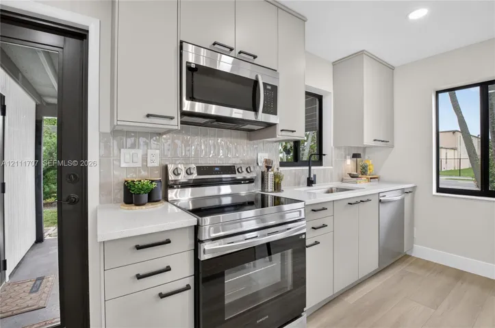 Kitchen featuring flat-panel beige cabinetry, stone-finish countertops, stainless steel appliances, a textured tile backsplash, and wood-finish flooring