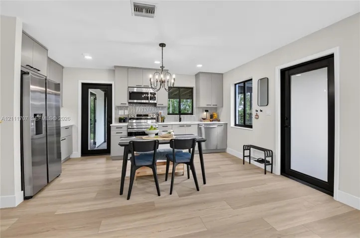 Kitchen featuring light-toned beige cabinetry, stainless steel appliances, wood-finish flooring, two exterior doors with black frames, and a multi-light chandelier