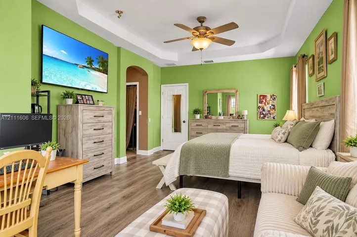Tray ceiling with a central multi-blade ceiling fan and wood-finish flooring