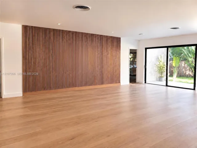 Expansive interior featuring wood-finish flooring, a floor-to-ceiling vertical wood slat accent wall, recessed lighting, and large sliding glass doors
