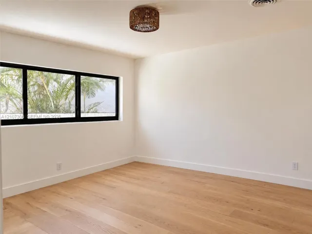 Neutral-toned interior featuring wood-finish flooring, a black-frame rectangular window, and a woven-textured flush-mount ceiling light
