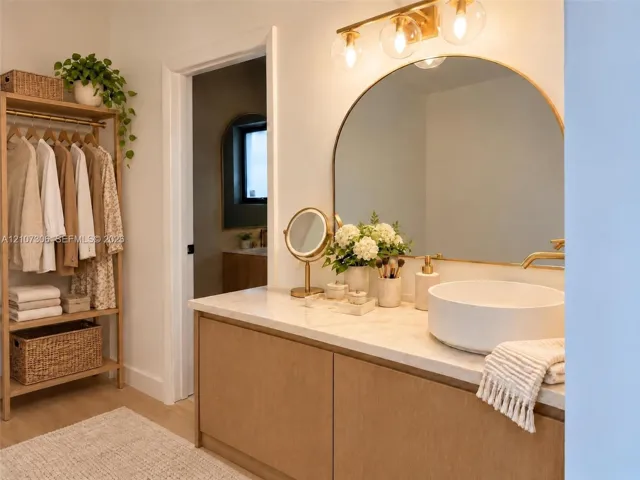 Custom wood-finish vanity with a neutral stone countertop, white vessel sink, arched wall mirror, and integrated gold-toned vanity lighting