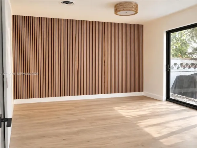 Vertical wood slat accent wall, light-toned wood-finish flooring, sliding glass door, and integrated circular drum lighting fixture