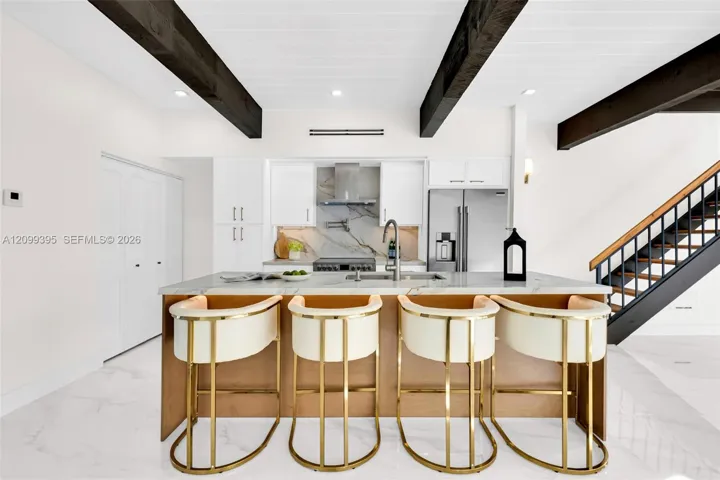 Kitchen featuring dark cedar wood-finish ceiling beams, white slim shaker-style cabinetry, stone-finish countertops, stainless steel appliances, and large-format tile flooring