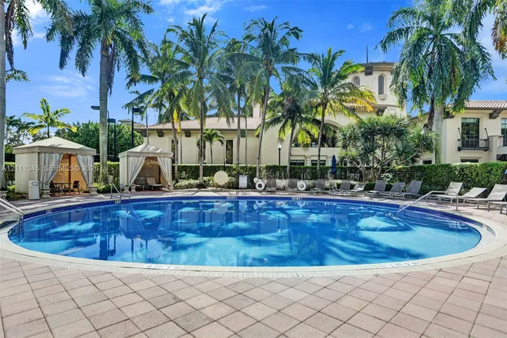 Circular swimming pool featuring a paved stone deck, dual shaded cabanas, and manicured palm tree landscaping