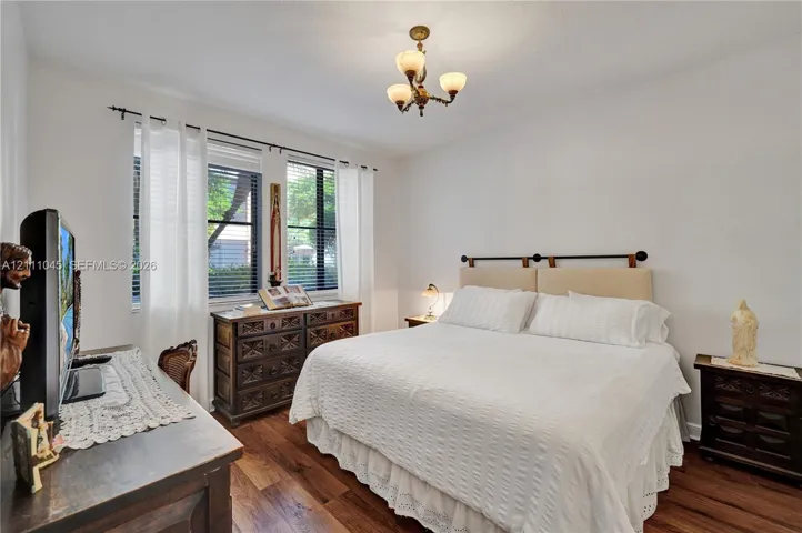 Bedroom featuring wood-finish flooring, dual windows with blinds, and a multi-arm chandelier