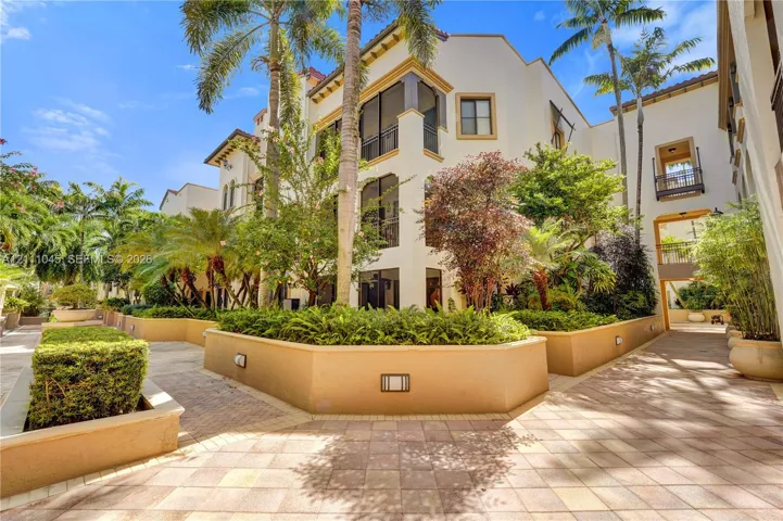 Mediterranean-style exterior featuring stucco facade, multi-level screened balconies, paver walkways, integrated landscape lighting, and raised masonry planters