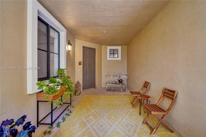 Covered entryway featuring textured stucco walls, a multi-pane window with black framing, a square accent window, and an attached exterior wall-mounted light fixture