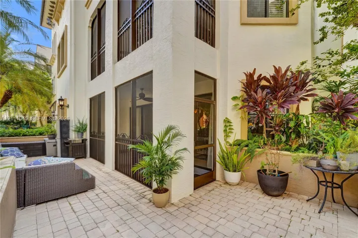 Stucco exterior featuring multiple levels, paved stone patio, screened enclosure, decorative metal railings, and attached exterior lighting