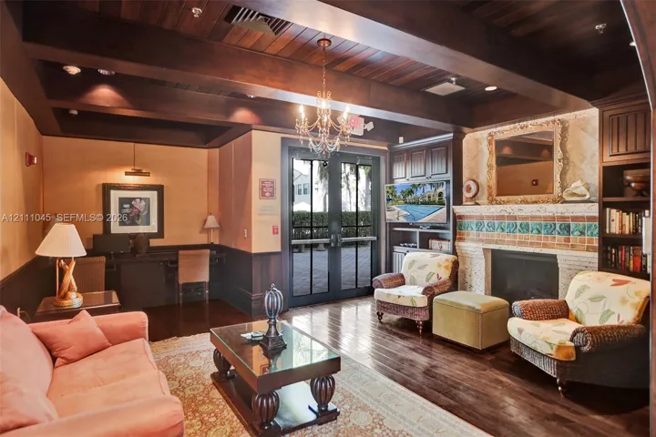 Wood-finish coffered ceiling with exposed beams, wood-finish flooring, masonry fireplace with decorative tile surround, built-in wooden cabinetry, and French-style glass paneled doors