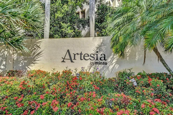 Community monument signage featuring dimensional lettering set against a smooth stucco wall, surrounded by mature palm trees and established flowering shrubbery