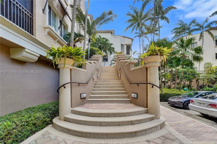 Exterior staircase featuring stone treads, stucco-finished retaining walls, decorative column accents topped with planters, and metal handrails