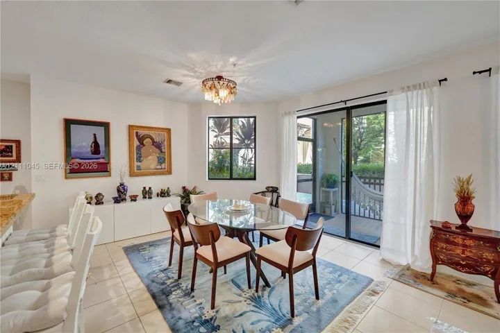 Dining area featuring large-format ceramic tile flooring, built-in cabinetry with a stone countertop, a decorative tiered chandelier, and sliding glass doors with access to a screened outdoor area