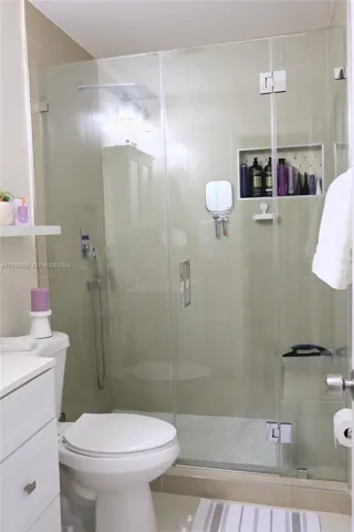 Bathroom 2 Walk-in shower featuring a seamless glass enclosure, rain-style showerhead, handheld sprayer, recessed wall niche, and tiled surround