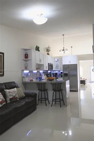 Kitchen featuring white shaker-style cabinetry, stone-finish countertops, stainless steel appliances, under-cabinet lighting, and large-format tile flooring