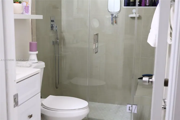 Batroom 2 Walk-in shower featuring a frameless glass door, wall-mounted chrome hand-held shower head, integrated tiled shower bench, and pebble-style floor tiling