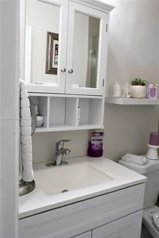 Bathroom 2 White vanity with a solid-surface countertop, integrated sink basin, chrome faucet, and mirrored cabinet featuring open display shelving