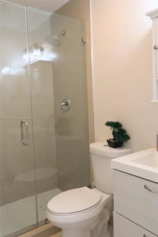 Bathroom 1 Frameless glass shower enclosure featuring a wall-mounted rainfall showerhead, chrome hardware, light-toned cabinetry with integrated basin, and neutral wall tile