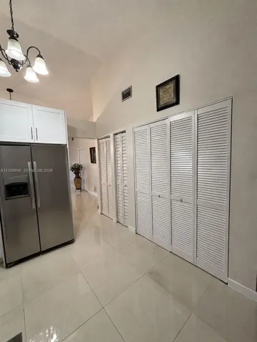 Vaulted ceiling, large-format tile flooring, stainless steel side-by-side refrigerator, white shaker-style upper cabinetry, and floor-to-ceiling louvered closet doors