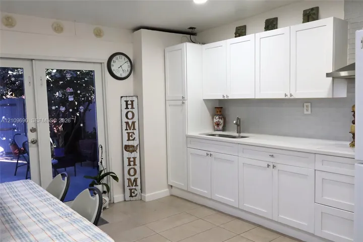 Kitchenette featuring white Shaker-style cabinetry, a stone-surface countertop, an integrated sink with a gooseneck faucet, a light-toned tile backsplash, and glass-paned double doors