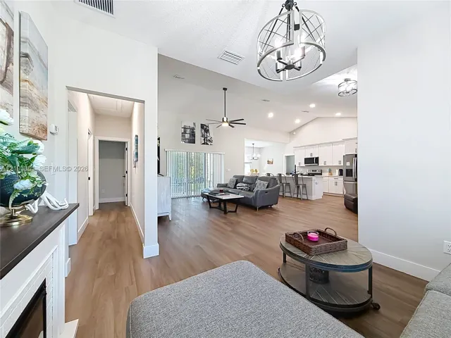 Open-concept interior featuring wood-finish flooring, vaulted ceilings, a metallic cage-style chandelier, white cabinetry, and recessed lighting