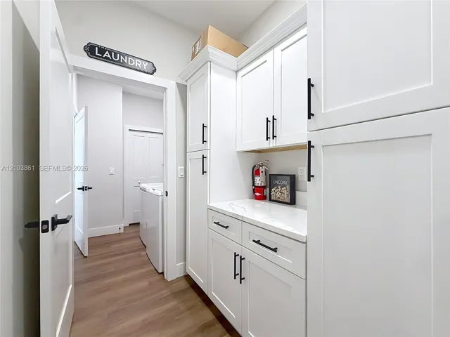 Custom white cabinetry featuring shaker-style doors, matte black hardware, and light-toned composite countertops, complemented by wood-finish flooring