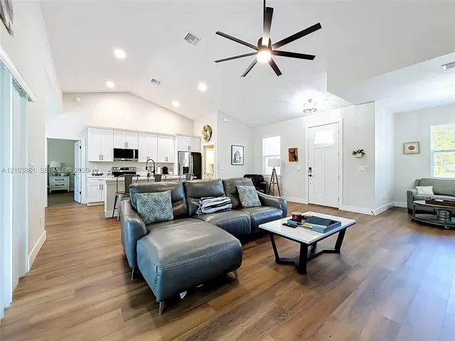 Open floor plan featuring vaulted ceilings, wood-finish flooring, recessed lighting, and a kitchen with white cabinetry and a center island