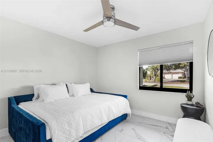 Neutral-toned room featuring large-format tile flooring with marble-style veining, a modern three-blade ceiling fan with an integrated light fixture, and a window equipped with horizontal cellular shades