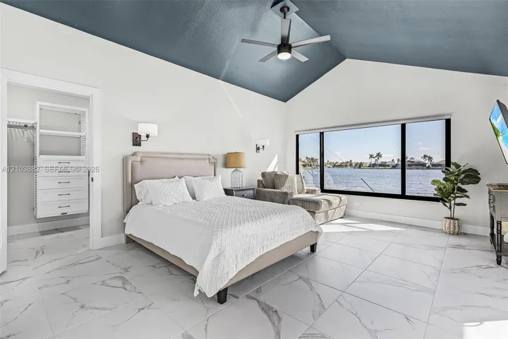 Vaulted ceiling with a matte-finish accent, large-format tile flooring with a stone pattern, floor-to-ceiling panoramic windows, built-in closet organization system, and wall-mounted light fixtures