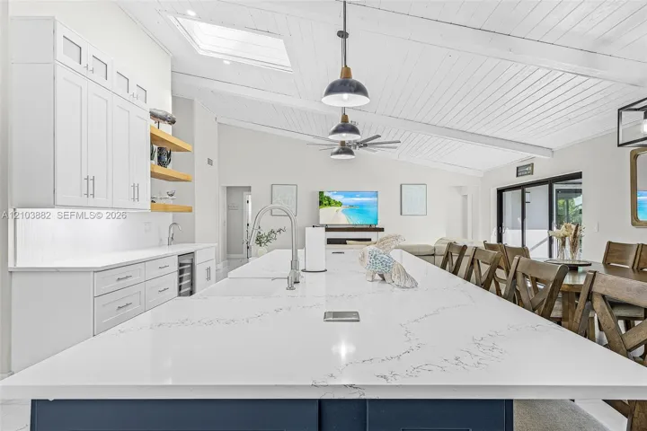 Kitchen featuring an oversized central island with stone-finish countertops, ceiling with exposed beams, skylights, matte black pendant lighting, and wood-finish cabinetry