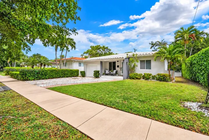 Single-story residence featuring a barrel tile roof, white stucco exterior, attached garage, stone-surfaced driveway, and landscaped shrubbery