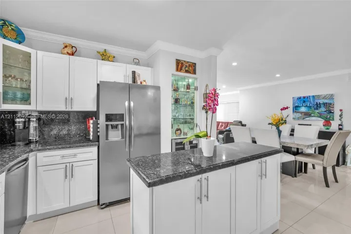 Kitchen featuring white shaker-style cabinetry, dark stone countertops, a central island, recessed lighting, and a built-in glass-front display cabinet