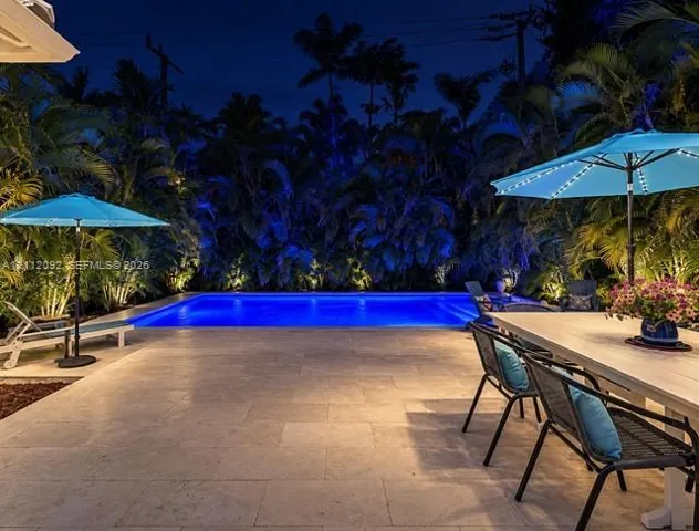 Rectangular inground swimming pool surrounded by a large stone paver patio and lush perimeter landscaping