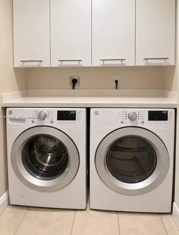 Laundry area featuring white cabinetry with brushed-metal pulls, solid-surface countertop, and ceramic tile flooring
