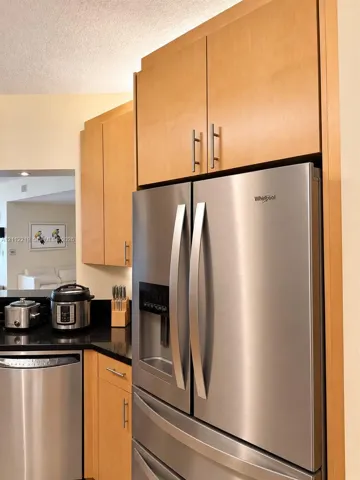 Kitchen featuring custom natural-tone cabinetry, stone-finish countertops, and stainless steel Whirlpool appliances including a French-door refrigerator and dishwasher