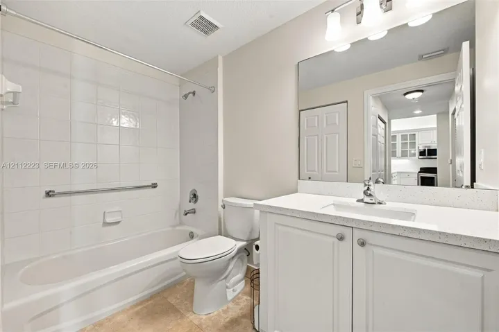 Bathroom featuring white cabinetry with a light-toned speckled countertop, an integrated rectangular sink, a large wall-mounted mirror, and a tub with tiled surround